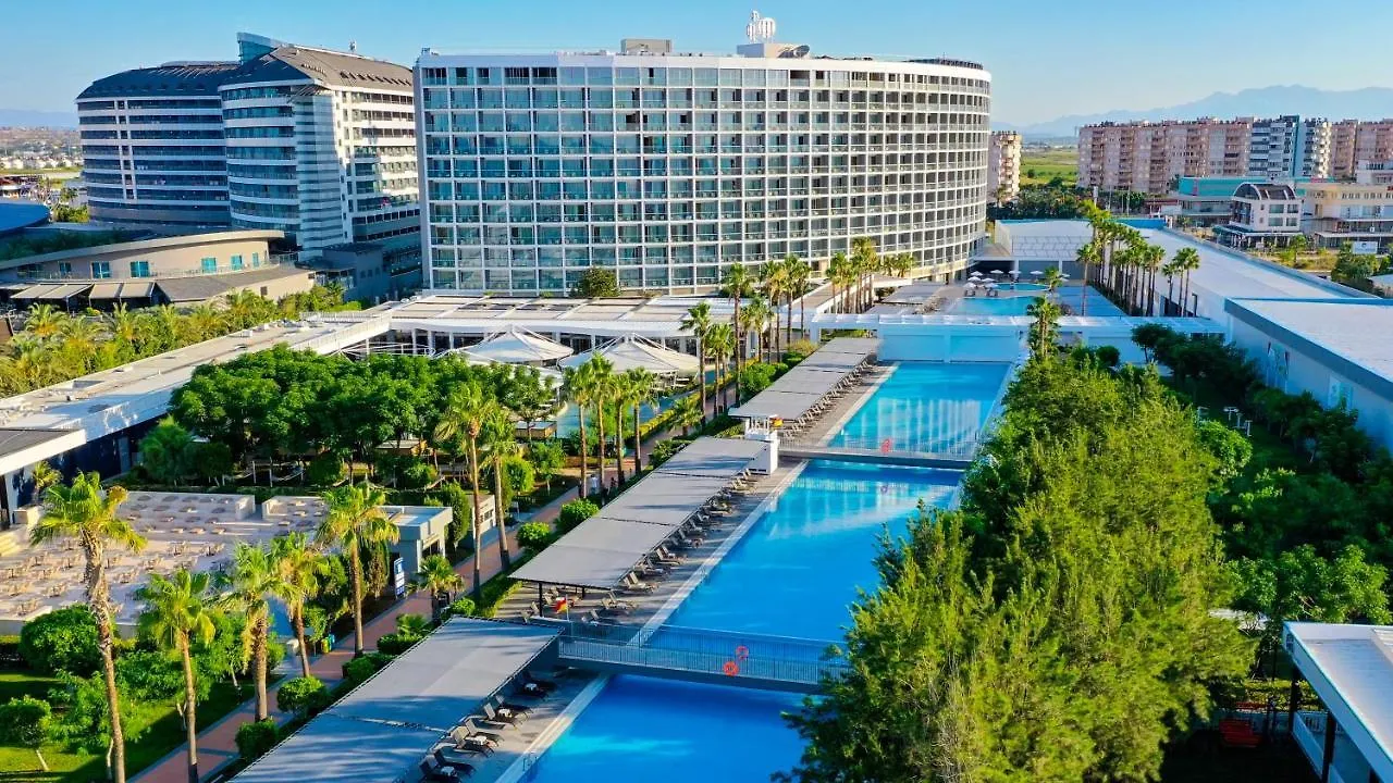 Crystal Centro Pearl Collection Hotel Antalya Amenities photo This is a vibrant, sunny photograph showcasing a large, modern hotel complex set within lush tropical landscaping.

The dominant feature is a massive, contemporary building in the background. It appears to be a high-rise hotel with a facade composed 